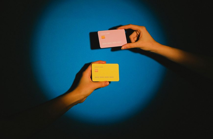 Two hands exchanging colorful credit cards under a spotlight against a vibrant blue background, symbolizing modern financial transactions.