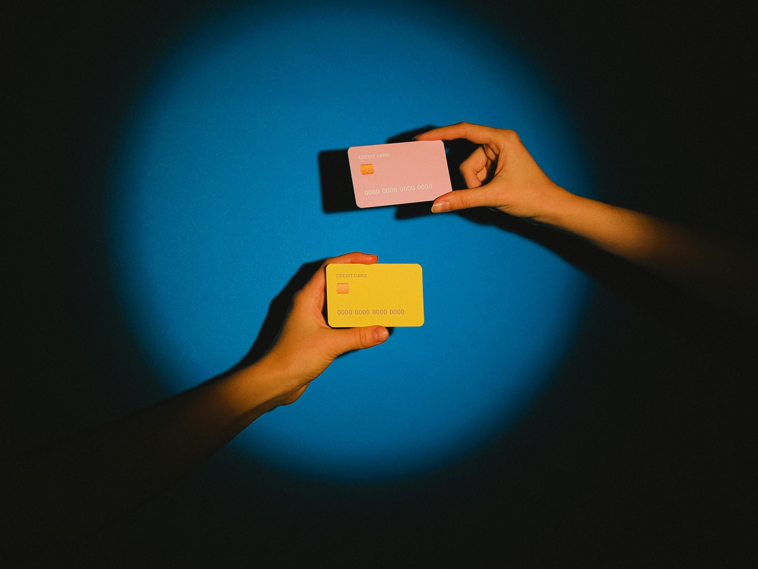 Two hands exchanging colorful credit cards under a spotlight against a vibrant blue background, symbolizing modern financial transactions.